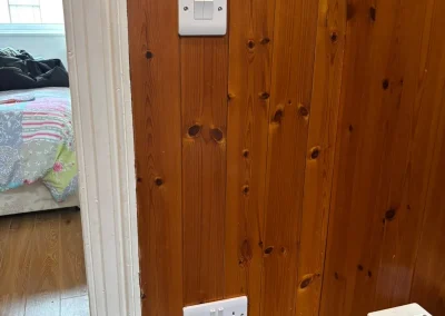 A white switch and socket on a timber-panelled wall.